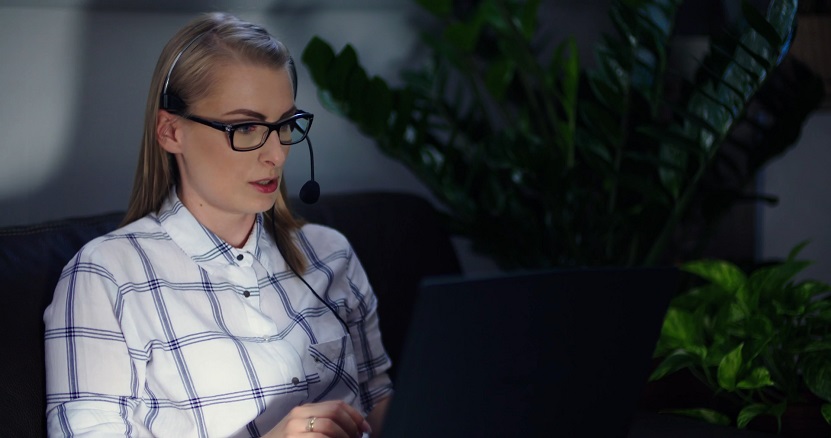Female interpreter wearing a headset and glasses, working remotely on a laptop during a video call