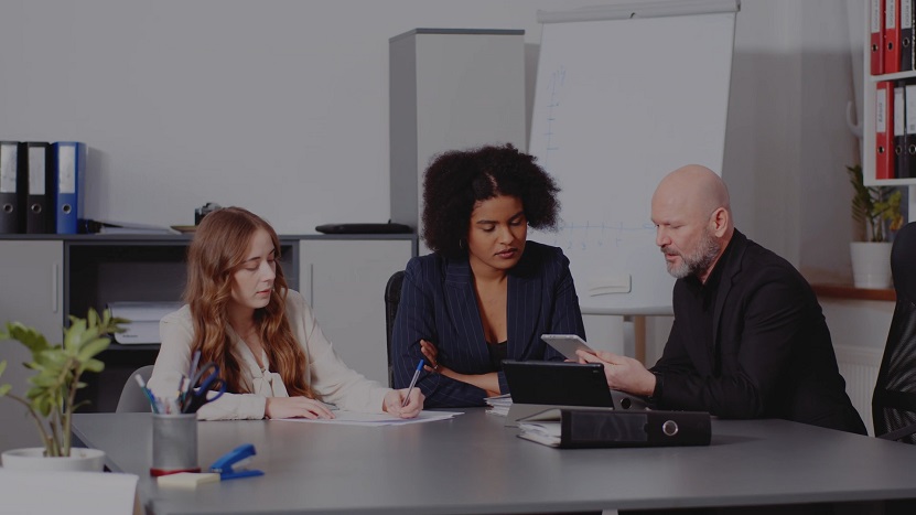 Team of three professionals in a formal meeting, discussing documents and digital data at the table