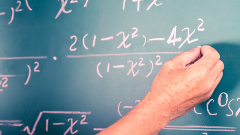 A hand writes equations on a chalkboard during a peer explanation session in math and physics