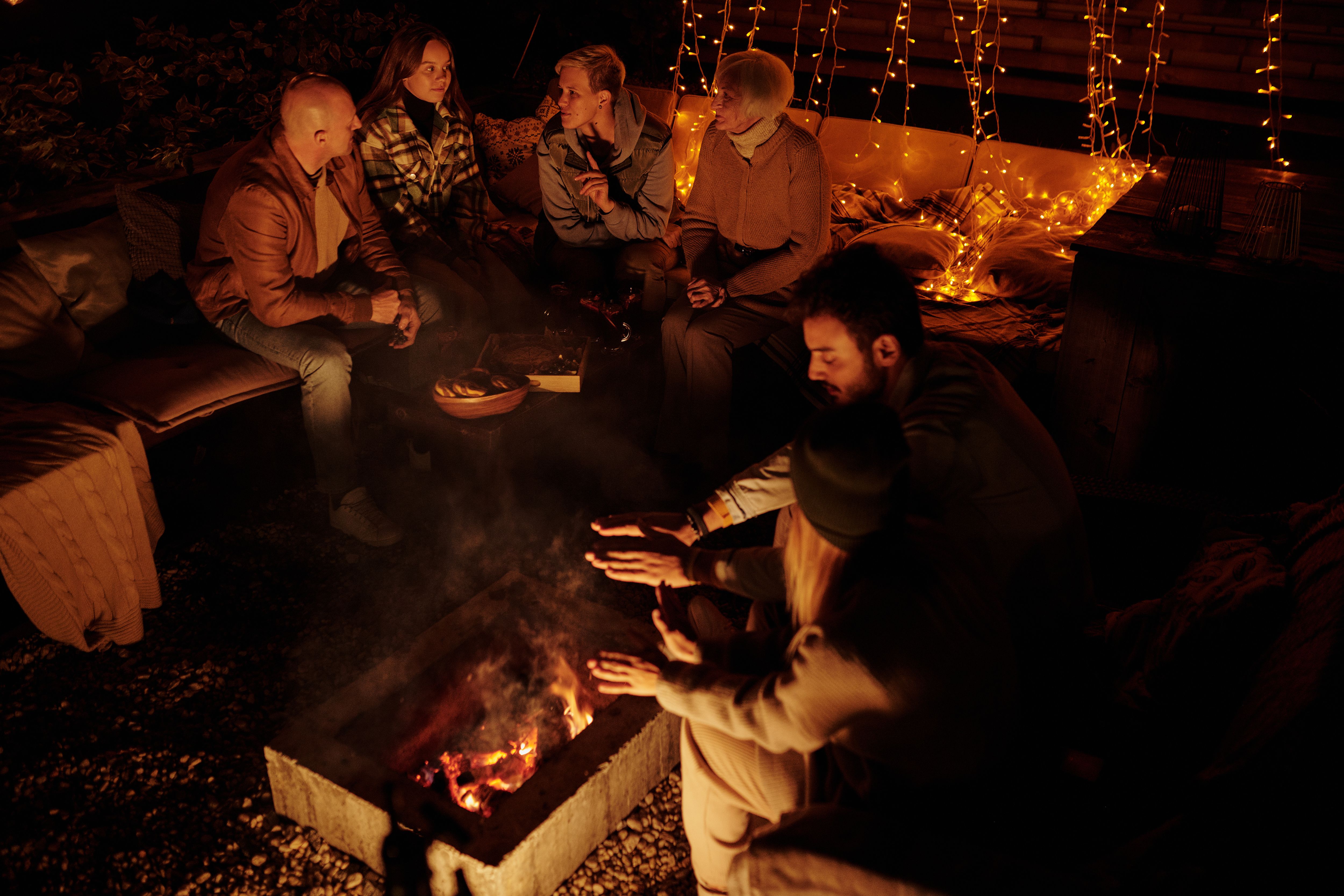 Friends gathered around a bonfire in a garden at night with glowing string garlands