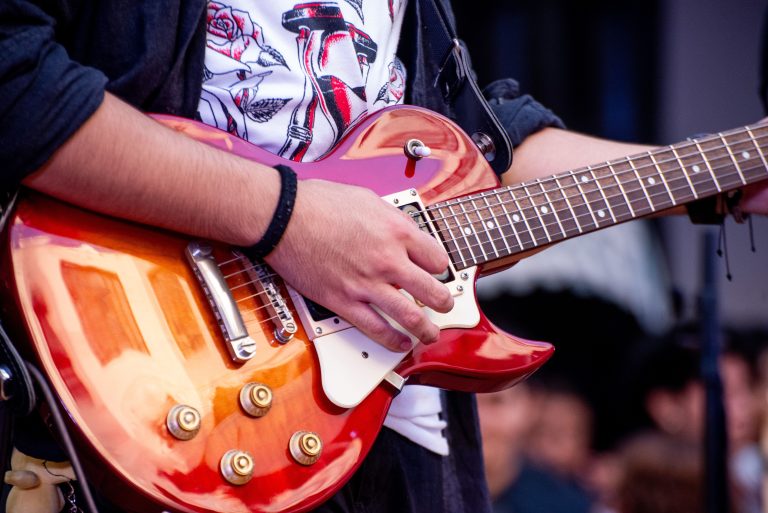Guitarist performing with a red electric guitar at an outdoor event